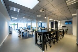 Modern ingericht kantoor aan de De Ruijterkade met flexplekken, hoge vergadertafel en grote ramen voor natuurlijk licht.